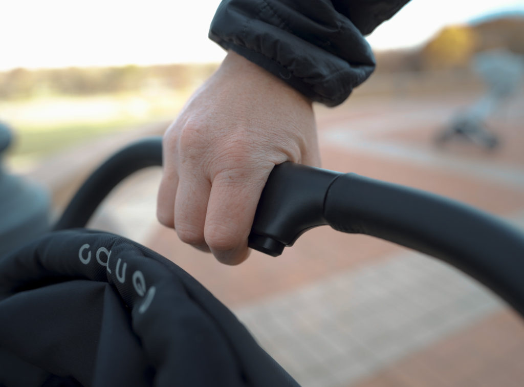 A hand demonstrating the Colugo Compact stroller's fold mechanism