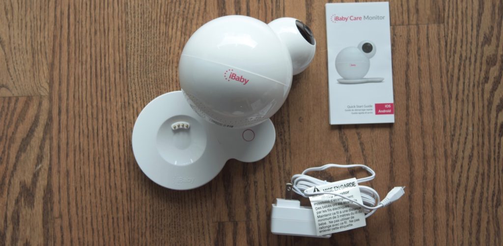 The iBaby M6S, its base, quick start guide and power cord on a hardwood floor