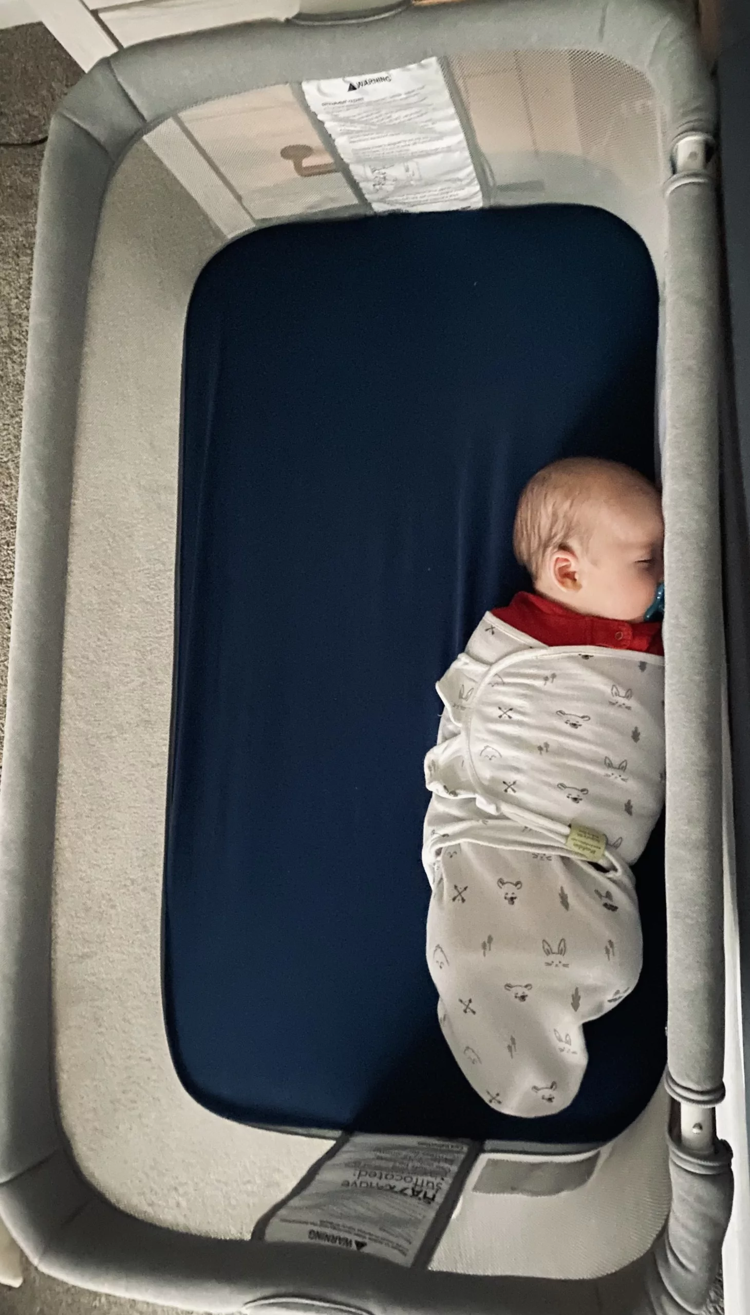 Swaddled sleeping newborn in Newton Bassinet with his face angled towards one of the mesh walls.