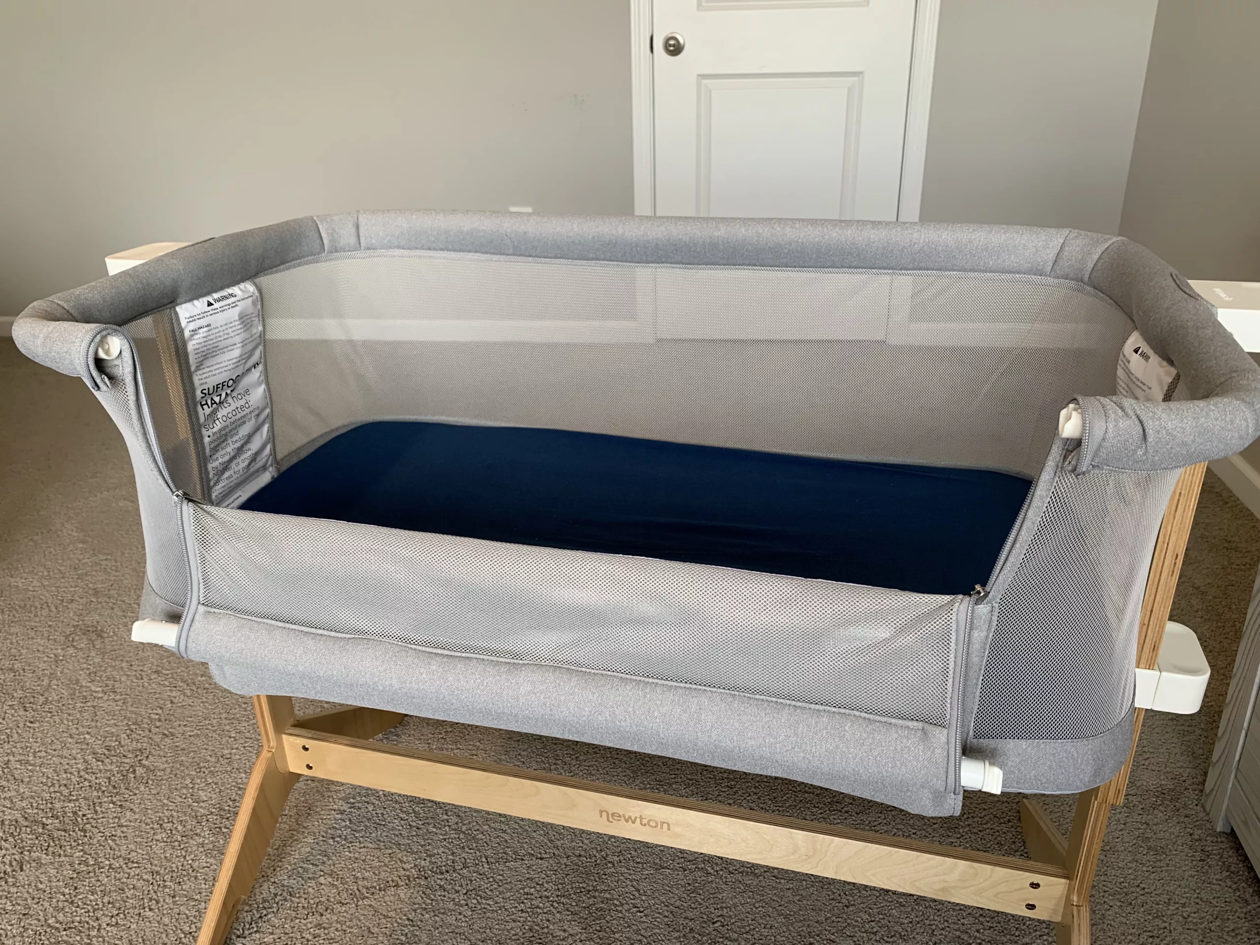 Side view of an empty Newton Baby Bassinet with blue sheets and the bedside sleeper wall rolled down.