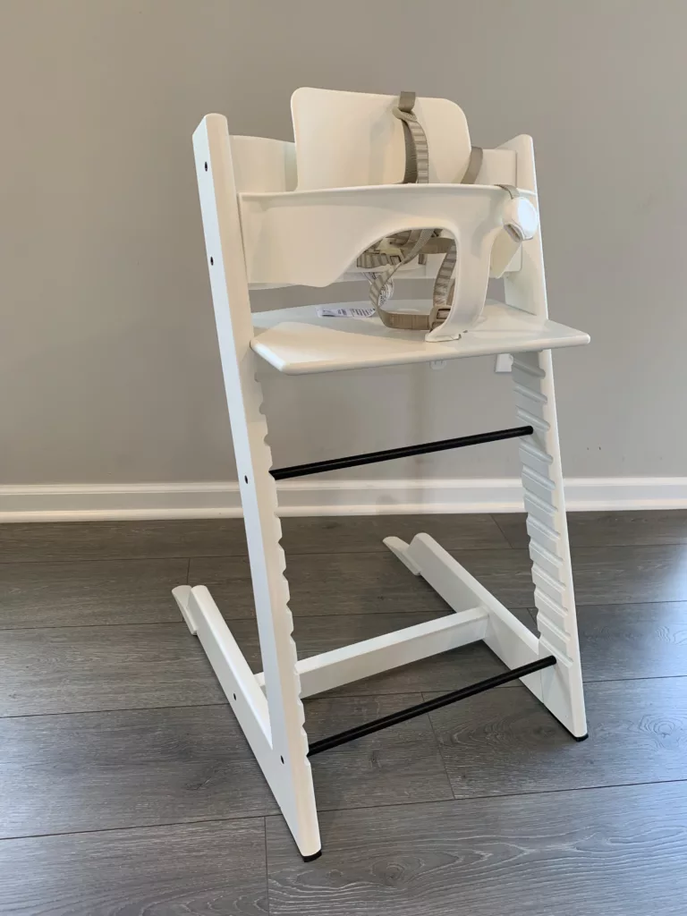 The image shows a white Stokke Tripp Trapp high chair, assembled with the baby set. It is unoccupied. 